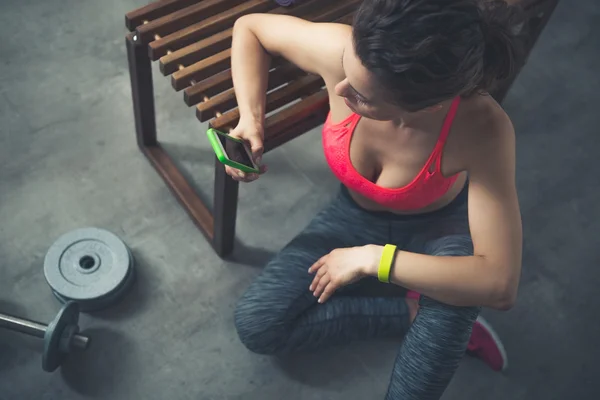 Fitness žena sedí v tělocvičně podkroví s mobilní telefon — Stock fotografie