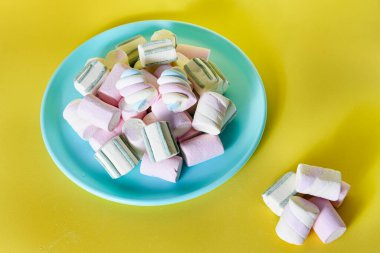 Sarı zemin üzerinde mavi bir tabakta tatlı marşmelovlar..