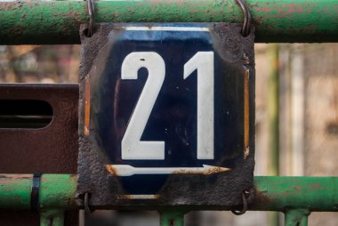 Yıpranmış, köhne, metal bir plaka. 21 numaralı sokak adresi.