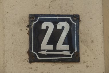 Yıpranmış, köhne, metal bir plaka. 22 numaralı sokak adresi.