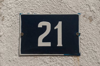 Yıpranmış, köhne, metal bir plaka. 21 numaralı sokak adresi.