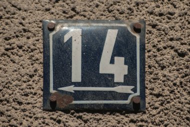 Yıpranmış, köhne, metal bir plaka. 14 numaralı sokak adresi.