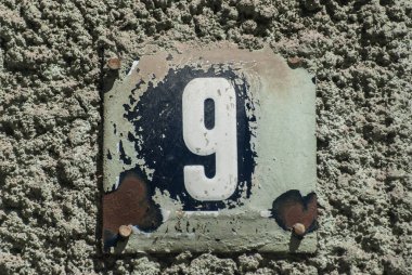 Yıpranmış, köhne, metal plakalı, üzerinde 9 numara olan sokak adresi.