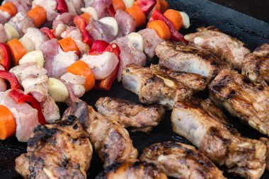 Raw pork skewers and grilled ribs cooking side by side on a hot barbecue grill, close-up view