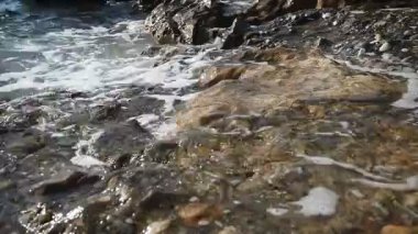 Sahil kayaları ve kumsalda yuvarlanan yumuşak dalgalar ve deniz köpüğü. Huzurlu Akdeniz kıyısı