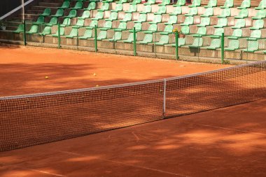 Tenis ağı sessiz bir kil sahası boyunca uzanır ve en az forma ve atmosfere odaklanmış bir spor sahnesi yaratır.
