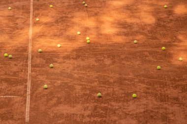 Boş bir kil kortunda çoklu tenis topu uzanır. Bu da antrenman yoğunluğunu ve spor hazırlıklarını yansıtır.