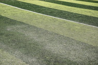 Doğal ışık altında mahallenin spor sahasında beyaz alan çizgileri olan yapay çim yüzeyi.