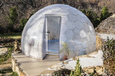 Açık havada jakuziyi kaplayan şeffaf polikarbonat kubbesi dağ villa bahçesinde, güneşli kış manzarasında modern spa barınağı