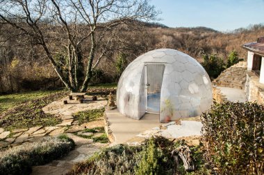 Açık havada jakuziyi kaplayan şeffaf polikarbonat kubbesi dağ villa bahçesinde, güneşli kış manzarasında modern spa barınağı