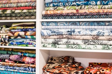 Terzilik atölyesi, tekstil seçimi ve moda tasarımı konseptinde düzgünce dizilmiş kumaşların olduğu raflar..