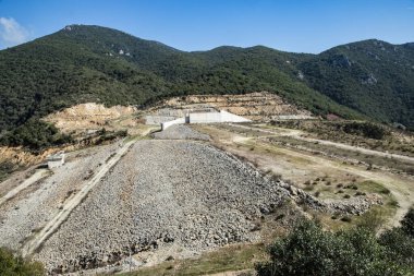 Dağlık arazide tamamlanmamış baraj inşaatı beton sızıntısı, mühendislik altyapı projesi ve çevresel etkiyi gösteriyor.