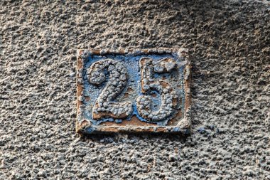 25 numaralı yıpranmış metal ev, duvarda klasik mimari detaylarını ve şehir sokak işaretlerini gösteren tabela..