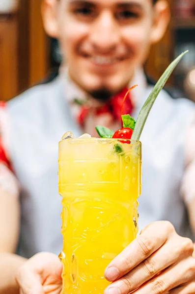 Barman met cocktail in een tiki glas op een bar toonbank op een wazige achtergrond van flessen in een bar. — Stockfoto