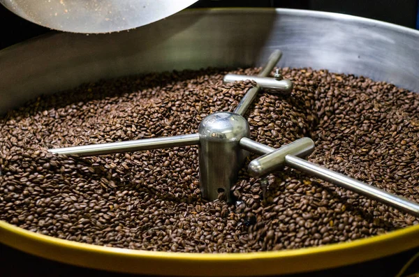 Grãos de café recém-torrados de uma grande torradeira de café moderna são mexidos no cilindro de resfriamento. — Fotografia de Stock