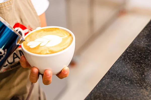 Hands of a Peruvian barista creates latte art in coffee shop
