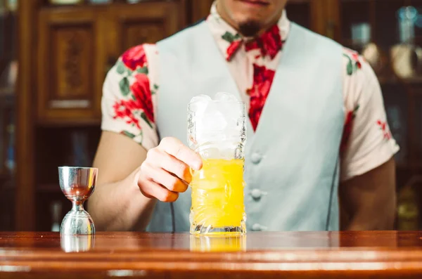 Barman ukazuje koktejl ve sklenici tiki na barovém pultu na rozmazaném pozadí lahví v baru. — Stock fotografie
