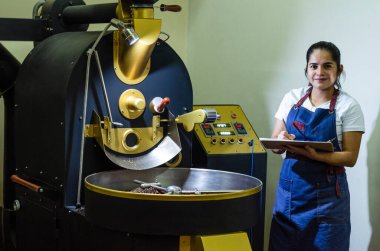 Bir kadın elleri, fasulye kızartmak için kullanılan modern bir makinede aromalı kahve çekirdeklerini kavurur..