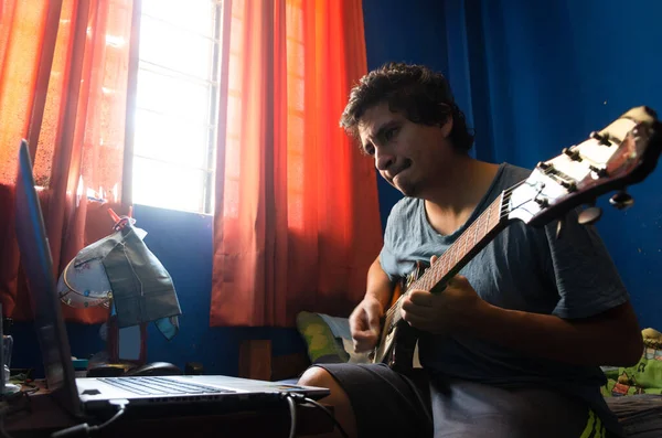 Hombre joven casual con guitarra y portátil en la cama en casa. — Foto de Stock