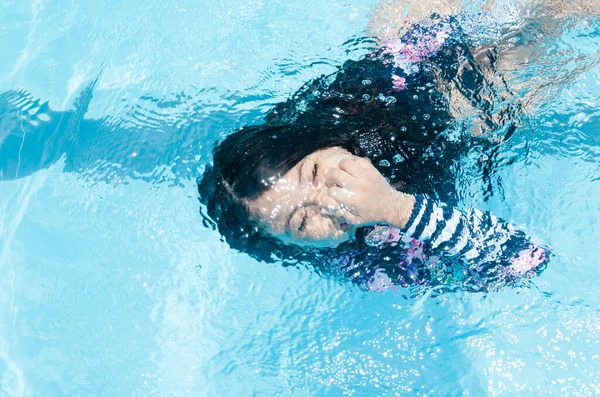 Het meisje in het zwembad dat onder water zwemt glimlachend en haar neus vasthoudt. — Stockfoto