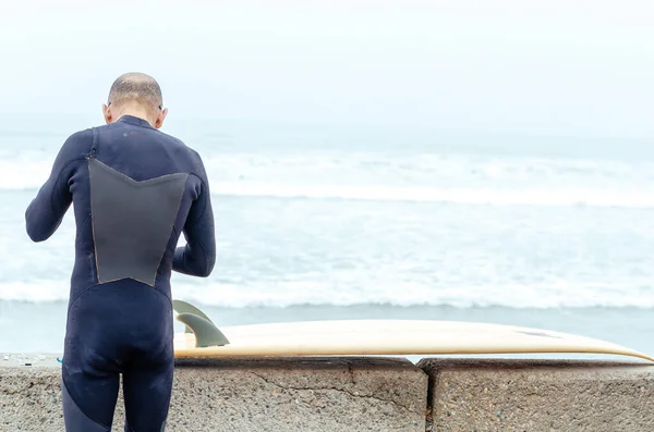 Sırtında sörf tahtası ve arkasında deniz olan yaşlı bir sörfçü.. — Stok fotoğraf