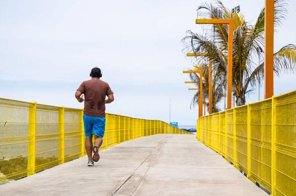 Un giovane uomo che ascolta musica e corre lungo la spiaggia vicino all'oceano al mattino. — Foto Stock