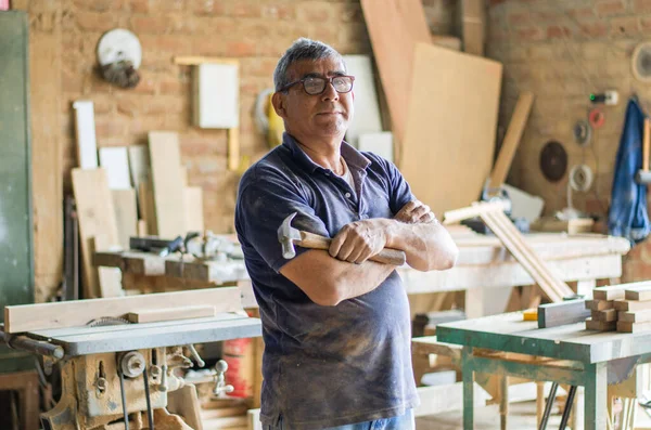 Anciano carpintero posando con los brazos cruzados en su taller. —  Fotos de Stock