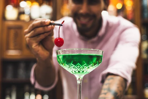 Jeune barman plaçant une cerise dans un cocktail vert, concept de soirée. — Photo