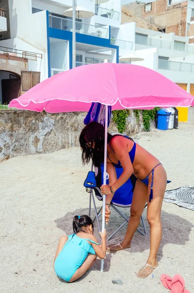 Madre e hija en una playa colocando sombrilla en la arena. —  Fotos de Stock