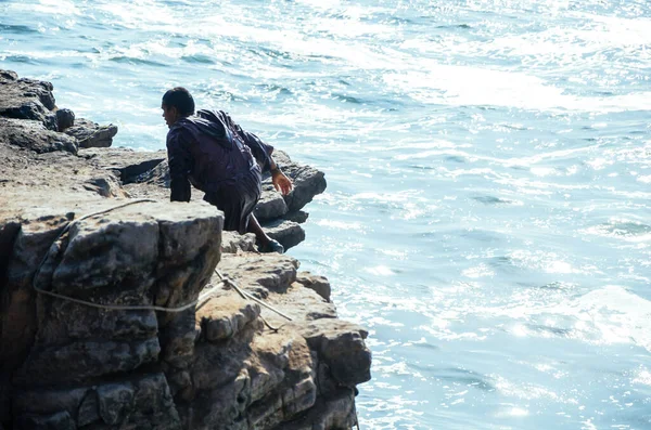 Man dressed as a friar throws himself off a cliff and head into the ocean at sunset. — Stock Photo, Image