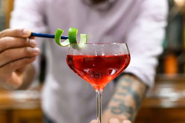 Zbliżenie szkła z czerwonym napojem, że barman dokładne ozdobić skórką pomarańczy. — Zdjęcie stockowe