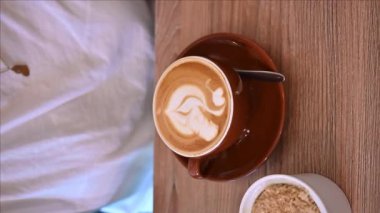 Bir fincan kapuçinoya nazikçe batırılmış bir çay kaşığı şeker hakkında. Kahvaltıda. Kahve molası. Kremalı kahve.