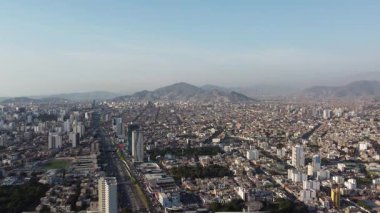 Arka planda yüksek binalar ve dağlar olan şehrin havadan görünüşü