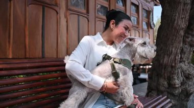 Halka açık bir parkta bankta oturan, gülümseyen ve onu okşayan neşeli genç bir kadın.