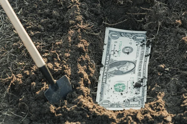 a shovel near the dug hole in it a dollar, bury the money in the ground. safety of money