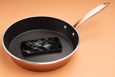 Kırık akıllı telefon siyah bir tavada, arka plan turuncusu