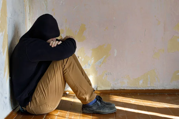 Bir adam dizlerini kıstırmış, depresyon ve yalnızlıkla yerde oturuyor. arkaplan duvarı duvar kağıdıyla