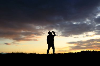 Gün batımına karşı içen bir adamın silüeti. Yalnızlık ve sarhoşluk kavramı