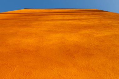 Binanın duvarı turuncuya doğru uzanıyor, aşağıdan görülüyor.