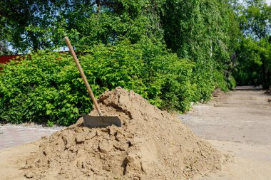 Kaldırımda bir kum dağı var, içine kürek yerleştiriliyor, yol onarımı yapılıyor.