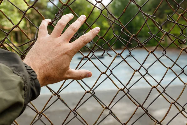 hand clings to the metal mesh fence. test of strength