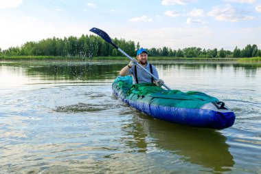 Kürek çeken bir kayıkta yelken açan bir adam, gökyüzü vahşi suya yansıyor.