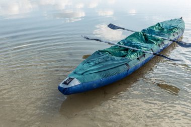 Gölde iki koltuklu şişme bir kano, insanlar olmadan, kürekler teknenin karşısında yatıyor. Su ve teknede yansıtan gökyüzü