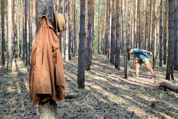 brown jacket in the foreground, in the background a man beats his head against a tree trunk. went into the forest to fight anger