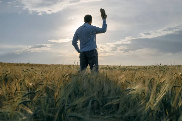 a man greets the dawn on the field with his hat raised in greeting. we meet a new day