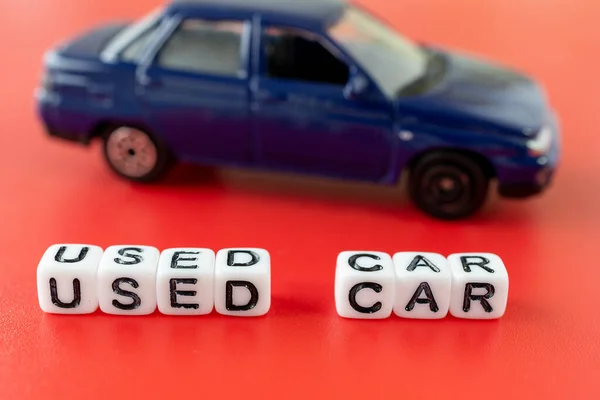 letters on the cubes make up the word used car, orange background on it blue toy car