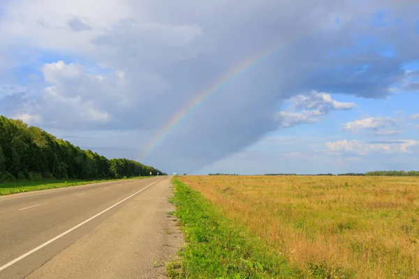 view from the side of the road and the rainbow above it. road stretching into the distance on a summer day