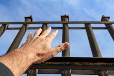 Bir adamın eli çitin tepesine ulaşır, özgürlük için can atar.