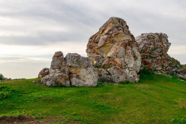 Gökyüzünün altındaki yeşil çimenlerdeki taşları ve bulanık sirrus bulutlarını. Yaz günü büyük kayalar