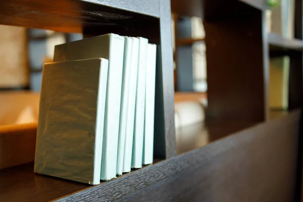 there are six covered books on a brown wooden shelf. decorative books